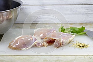 Three skinless chicken thighs on a cutting board with herbs