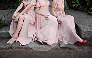 Three slender young girls in pink dresses are sitting on the stairs outside.