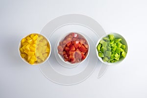 Three small bowls of chopped paprika with spread pieces of mixed paprika on the background