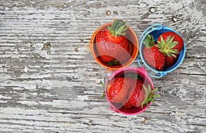 Three small colorful buckets full of strawberry