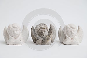 Three small identic handmade stone gyps angels on white background.