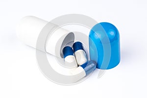 Three small pills are coming out from big blue and white capsule