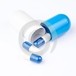 Three small pills are coming out from big blue and white capsule