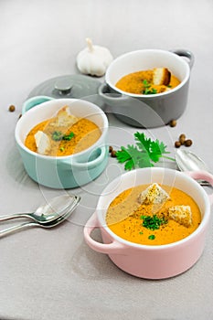 Three small serving pots or bowls with cream soup made of red lentils with rusks, spices and herbs parsley, coriander