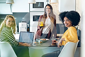 Three smart entrepreneur women talking while taking a break and having a breakfast while looking at camera in the kitchen at