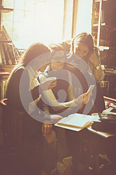 Three smiley students girl in cafe using smart phone.