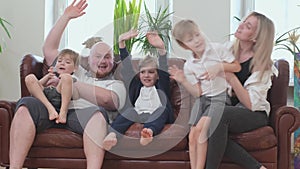 Three smiling boys and happy parents waving at the camera sitting on sofa