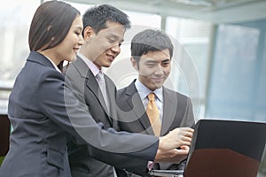 Three smiling business people looking at laptop and pointing, indoors