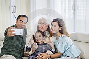 Three smiling generation family takes selfie at home