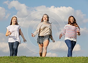 Three smiling girls run at grass