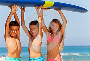 Three smiling kids boys and girl carry surfboard