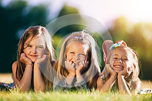 Three smiling little girls laying on the grass in the park.