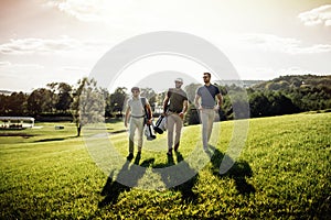 Three smiling men in sunglasses holding golf clubs outdoors