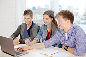 Three smiling students with laptop and notebooks