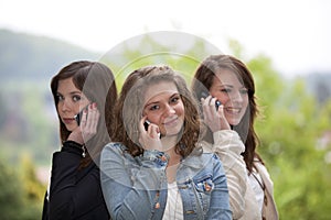 Three smiling teenagers with cellphones