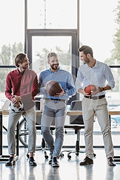 three smiling young businessmen holding basketball soccer and rugby balls