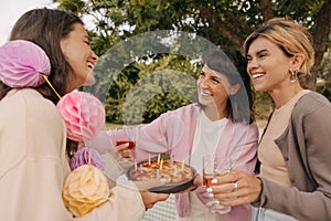 Three smiling young caucasian girls celebrate birthday together in nature on summer day.