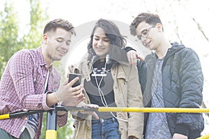 Three smiling young people talk and have great fun. Viewing images on your mobile phone.