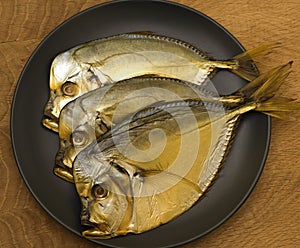 Three smoked vomer fish, lie on a black plate, on a wooden board