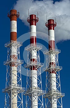 Three Smoking factory pipes with smoke on blue sky background