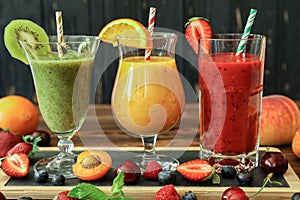 Three smoothies from different fruits and berries such as kiwi, orange, peach, apricot, cherry, strawberry, raspberry