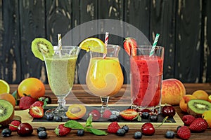 Three smoothies from different fruits and berries such as kiwi, orange, peach, apricot, cherry, strawberry, raspberry