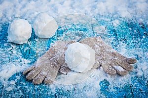 Three snowflakes and mittens on a snow-covered blue wooden surface
