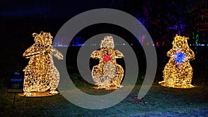three snowman statues lit up for the night near some lights