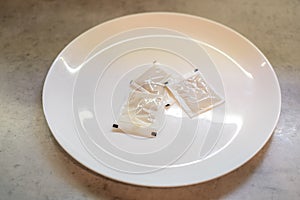 Three spice packets placed white plate. Each sealed, contents concealed. Arrangement aligned evenly, packaging intact photo
