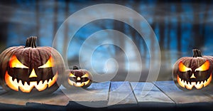 Three spooky halloween pumpkins, Jack O Lantern, with evil face and eyes on a wooden bench