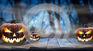 Three spooky halloween pumpkins, Jack O Lantern, with evil face and eyes on a wooden bench