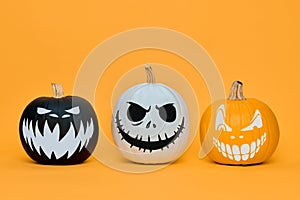 Three Spooky Halloween pumpkins with scary face expressions over orange background. Halloween concept.