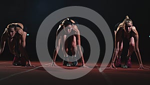 Three sports girl athletes at night on the treadmill start for the race at the sprint distance from the sitting position