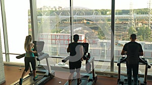 Three sports people, two men and woman running on treadmills in a gym