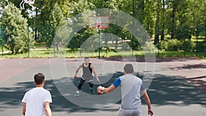 Three sportsmen playing basketball on the court outdoors - man in black uniform throwing the ball