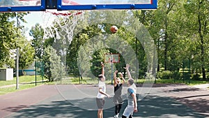 Three sportsmen playing basketball on the court outdoors - man in black uniform throwing the ball and scoring