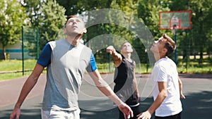 Three sportsmen playing basketball on the court outdoors - one man throwing the ball