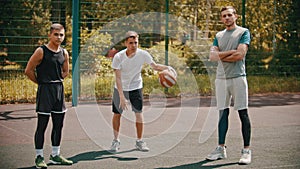 Three sportsmens standing on the basketball court outdoors and looking in the camera