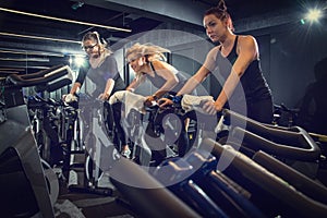Three sporty girls riding exercise bikes together on cycling training at gym