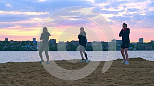 Three sporty young female boxers train on the beach at sunset in the evening