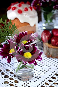 Three spring flowers. Easter cake and red coloured eggs in the background.