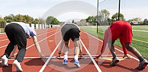 Three sprinters in the set position from behind ready to run down the track