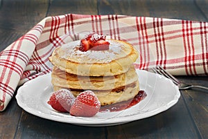 Three stacked pancakes with fresh strawberries on a vintage wood
