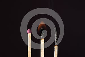 Three stages of burning matches on a dark background.