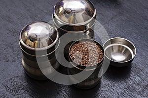 Three stainless steel containers two of them closed and one open full of flak seeds on a black wooden table