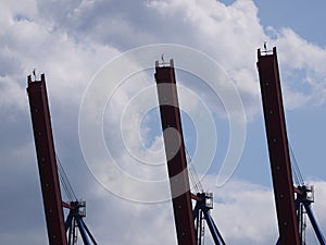 Three steel, rust-painted, outriggers of harbor cranes.