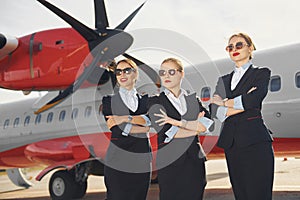 Three stewardesses. Crew of airport and plane workers in formal clothes standing outdoors together