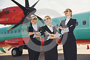 Three stewardesses. Crew of airport and plane workers in formal clothes standing outdoors together