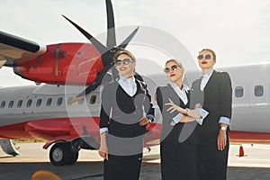 Three stewardesses. Crew of airport and plane workers in formal clothes standing outdoors together