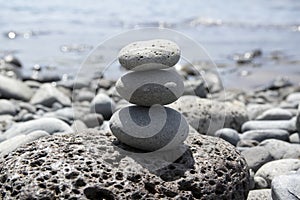 Three stone cairn tower on Madeira seacoast, poise stones, rock zen sculpture, light grey pebbles, blue ocean background